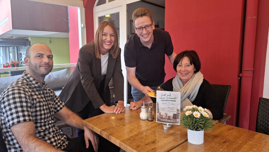Pfarrer Christian Schäfer (2. von rechts) bedient die Café-Besucherin Gisela Plesse. Ebenfalls im Bild: Die Inhaber des Allee Cafés, Christoph Neumeyer und Ina Kregelius.