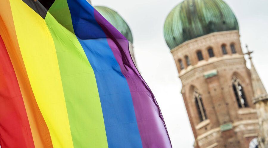Eine Regenbogenflagge, dahinter die Frauenkirche in München. Foto: IMAGO / Wolfgang Maria Weber