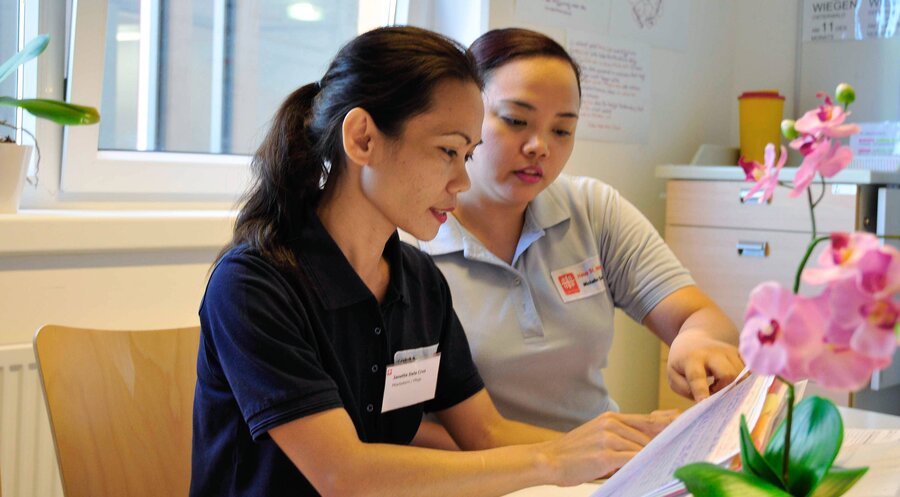 Pflegerin Janette Dela Cruz (l.) von den Philippinen wird in einem Altenheim der Caritas von einer Kollegin eingewiesen. Foto: IMAGO/epd