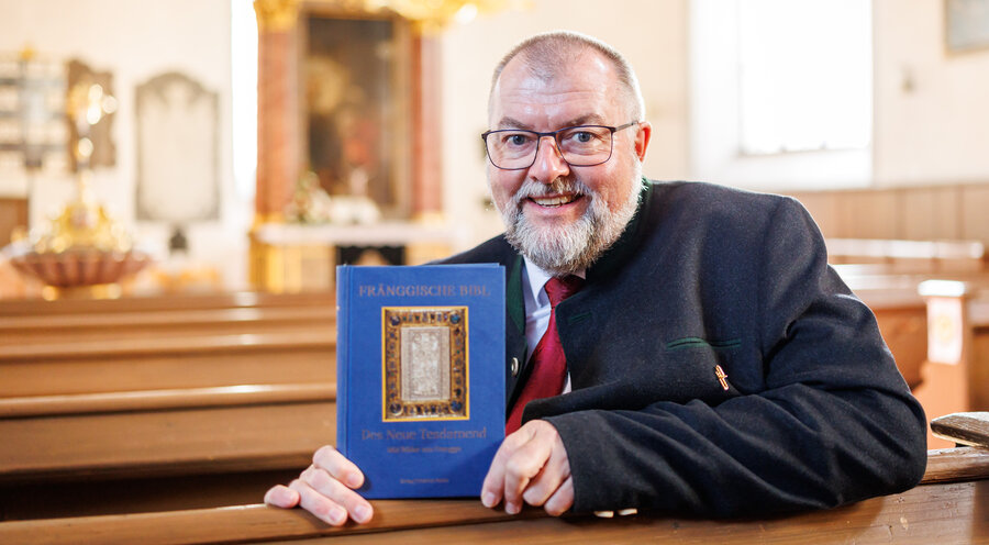 Pfarrer Claus Ebeling hält „Die Fränggische Bibl - Des Neue Tesdamend“ in der evangelischen Dreieinigkeitskirche in den Händen. Foto: picture alliance/dpa | Daniel Karmann