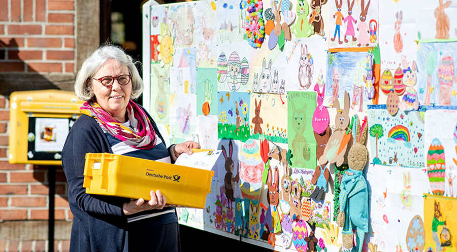 Doris Kröger, Mitarbeiterin im Osterpostamt, steht am Gemeindehaus vor einer Stellwand mit zahlreichen Briefen, die Kinder für den Osterhasen Hanni Hase geschrieben und gemalt haben. Foto: picture alliance/dpa | Hauke-Christian Dittrich