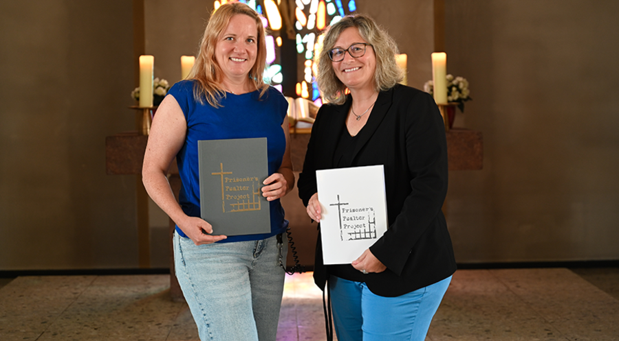 Pfarrerin Julia Held (l.) und JVA-Leiterin Mareike Knappik präsentieren in der Kirche der JVA Butzbach das fertige Buch „Prisoner’s Psalter Project“. 